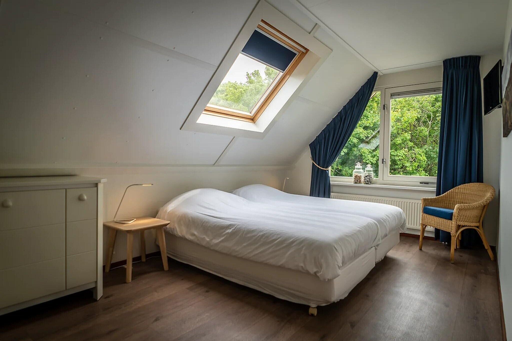 Ein Schlafzimmer mit Oberlicht, einem Bett, einem Sessel und einem Fenster mit Vorhängen.