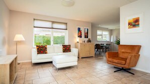 Ein modernes Wohnzimmer mit einem weißen Sofa, einem braunen Sessel, einer Holzkommode und einem Essbereich im Hintergrund.