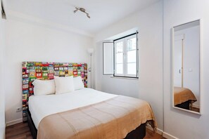 Ein Schlafzimmer mit einem Bett, einem Fenster, einem Spiegel und einer Wand mit farbigem Muster.