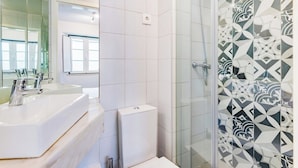 Et badeværelse med et stort spejl, to håndvaske, et toilet og en bruseniche med mønstret fliser.