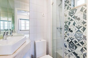 Ein Badezimmer mit großem Spiegel, zwei Waschbecken, Toilette und Dusche mit gemusterten Fliesen.
