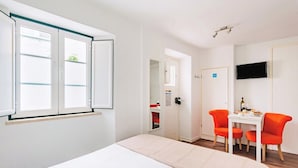 Et hotelværelse med en seng, et skrivebord med to stole, et fjernsyn og en dør til et badeværelse.