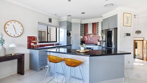 Een moderne keuken met een centraal eiland, barkrukken en een klok aan de muur.
