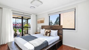 Een hotelkamer met een groot bed, een raam met uitzicht op een bakstenen gebouw en een balkon met plantenpotten.