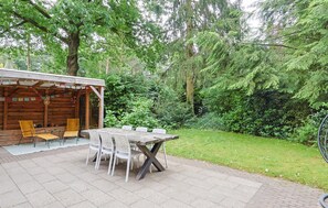 Una cabana de fusta amb una zona de terrassa que inclou una taula i cadires, envoltada de vegetació exuberant.