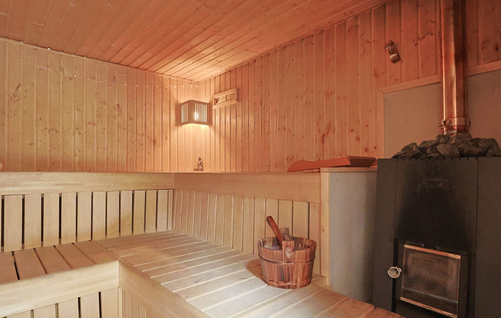 Un sauna en bois avec des bancs, un luminaire fixé au mur et un poêle à bois.