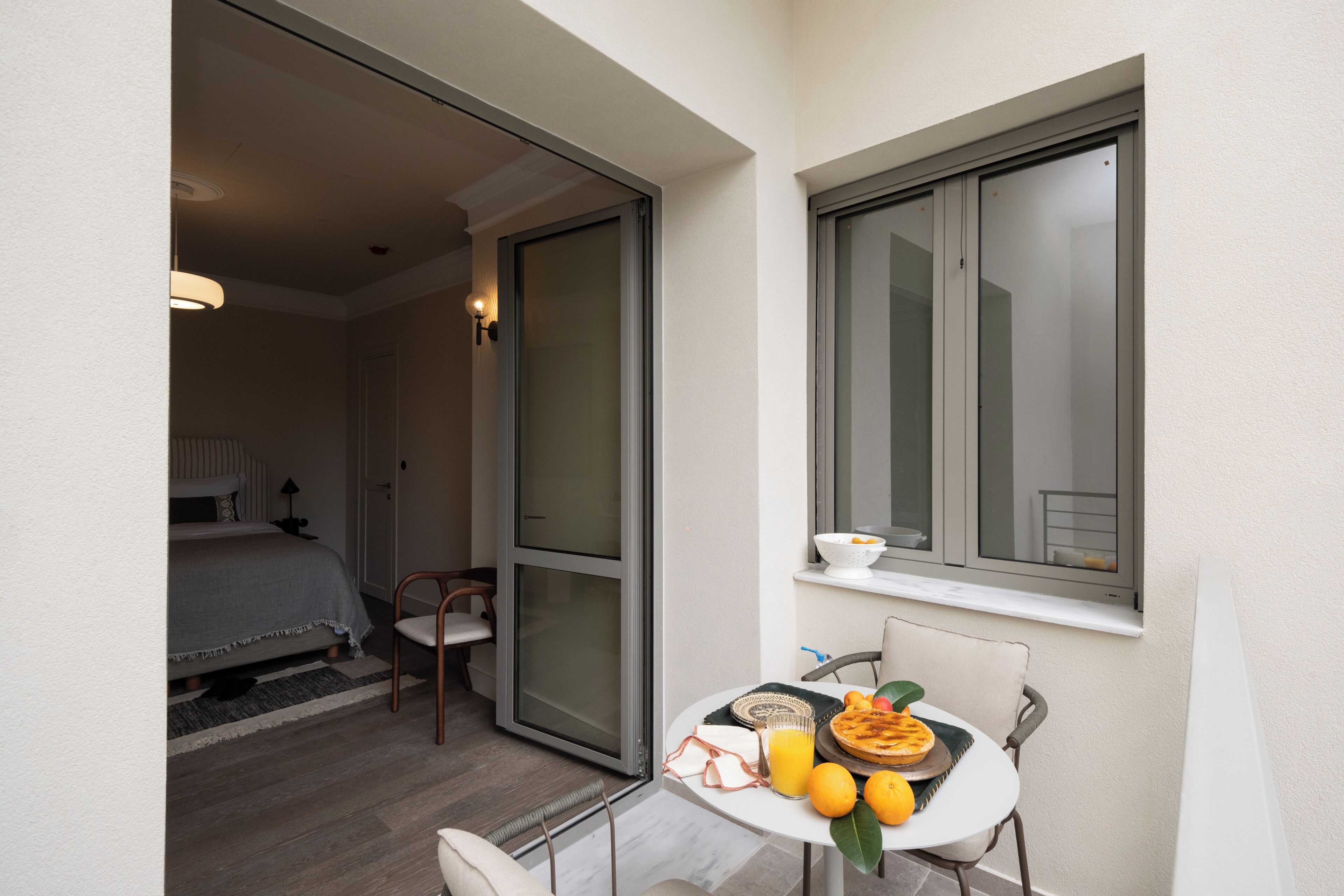 A small balcony with a table set for breakfast, a chair, and a window with a view.