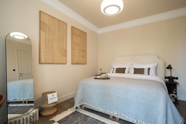 A bedroom with a bed, a bedside table, a lamp, a mirror, and two wall-mounted artworks.
