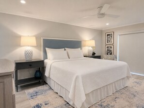A bedroom with a bed, two bedside tables, a nightstand, a ceiling fan, and a door. - Harbour Light Towers 1702 Beachfront and Renovated (Clearwater Beach)