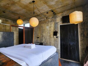 A hotel room with a large bed, two hanging paper lanterns, a wooden headboard, a black door, and a concrete ceiling. - MOD HOTEL CHIANG MAI (Chiang Mai)