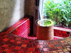 Rincón con suelo de baldosas rojas, una mesa de vidrio y plantas verdes.