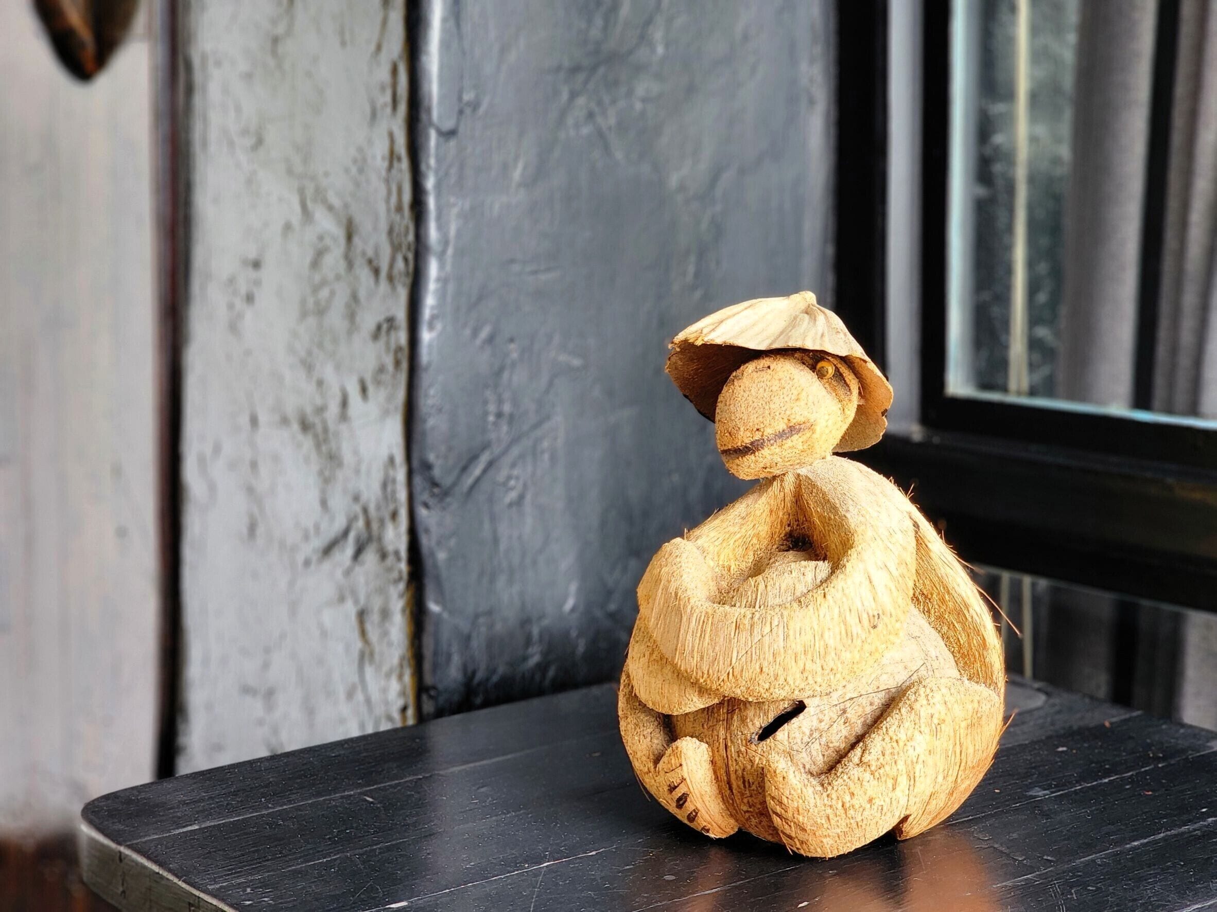 A sculpture of a figure seated on a dark wooden surface.