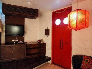 Una habitación con una televisión montada en un mueble de madera, una puerta roja con un ventanal circular y un farolillo rojo tradicional colgando del techo.