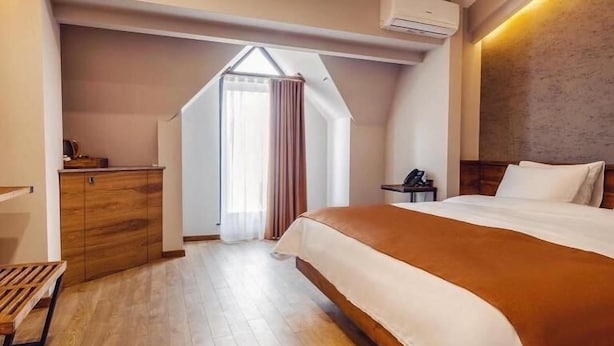 A bedroom with a large bed, wooden flooring, a desk, and an air conditioning unit.