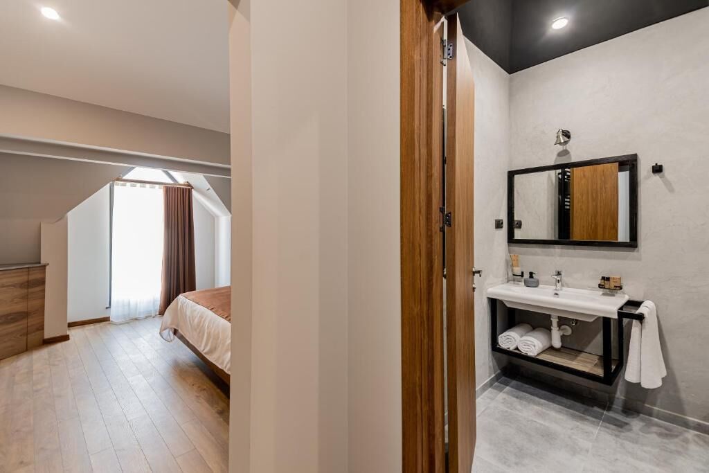 A modern bedroom with a wooden wardrobe, a large bed, a skylight, and a bathroom with a mirror and sink.