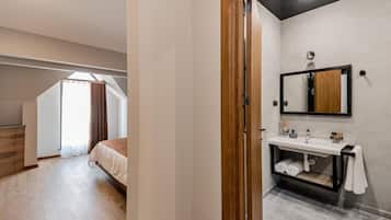 Un dormitorio moderno con un armario de madera, una cama grande, un tragaluz y un baño con espejo y lavabo.