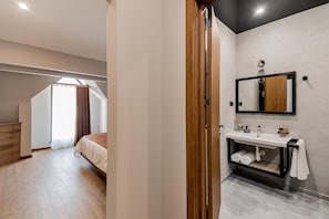 A modern bedroom with a wooden wardrobe, a large bed, a skylight, and a bathroom with a mirror and sink. - Ivy Hotel Tbilisi (Tbilisi)