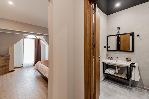 A modern bedroom with a wooden wardrobe, a large bed, a skylight, and a bathroom with a mirror and sink. - Ivy Hotel Tbilisi (Tbilisi)