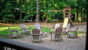 Een terras met Adirondack-stoelen en een vuurkuil van steen.