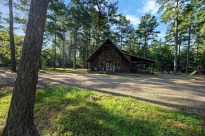 Eine Lodge mit einer großen Veranda, umgeben von hohen Bäumen und einer Schotterzufahrt.