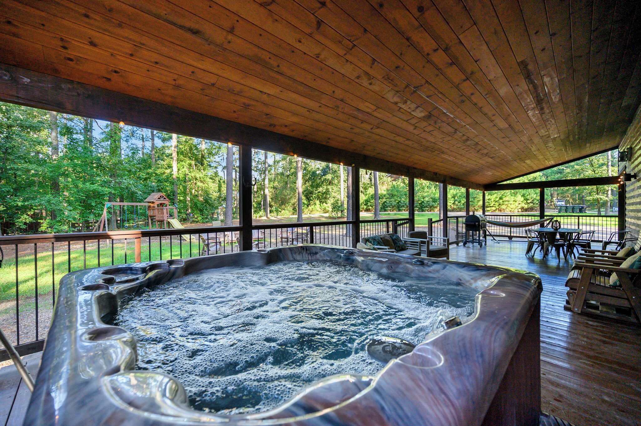 Un jacuzzi en una terraza de madera con vista a un área boscosa.
