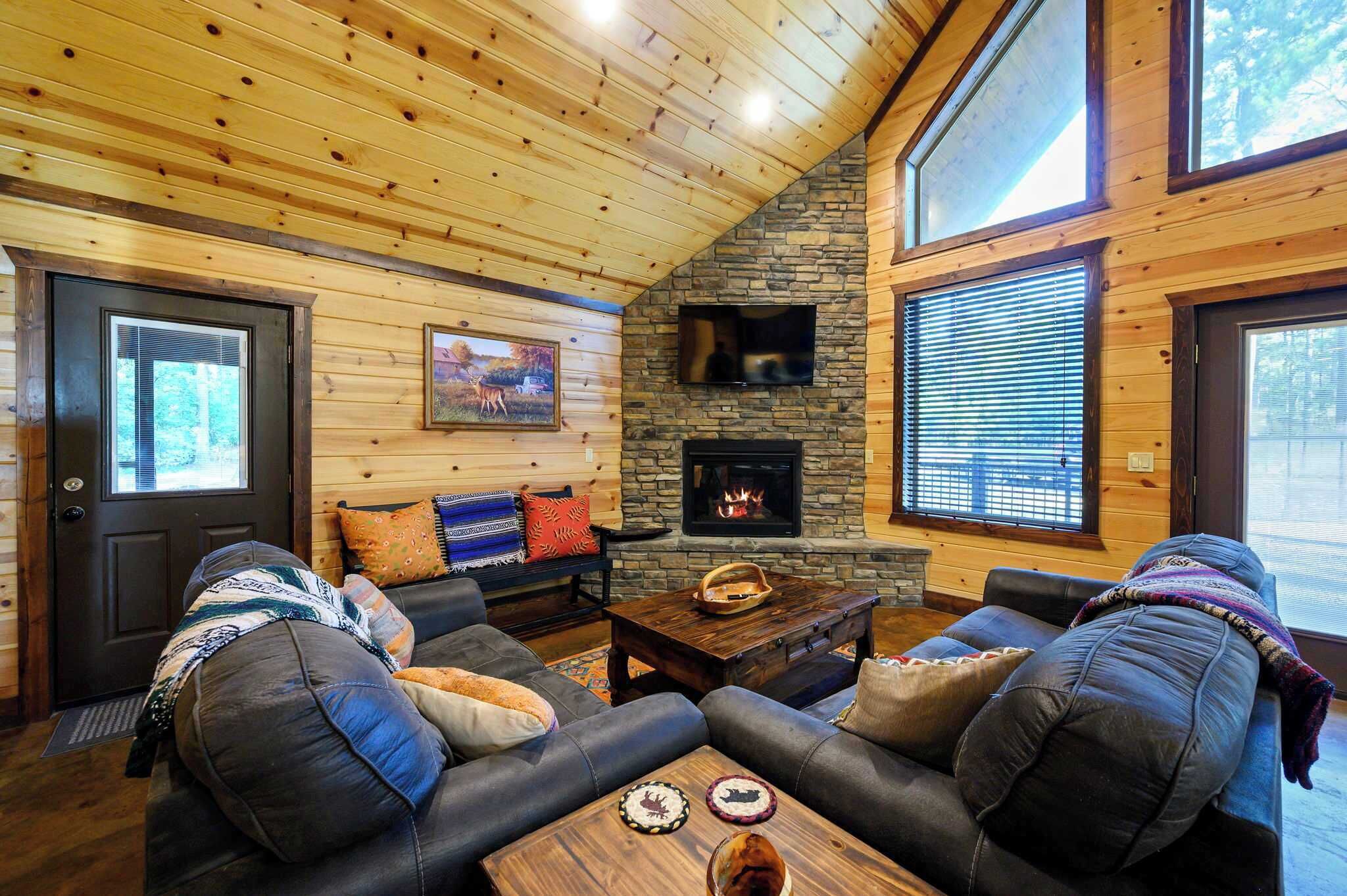 A cozy living room with a stone fireplace, leather sofas, and a large window.