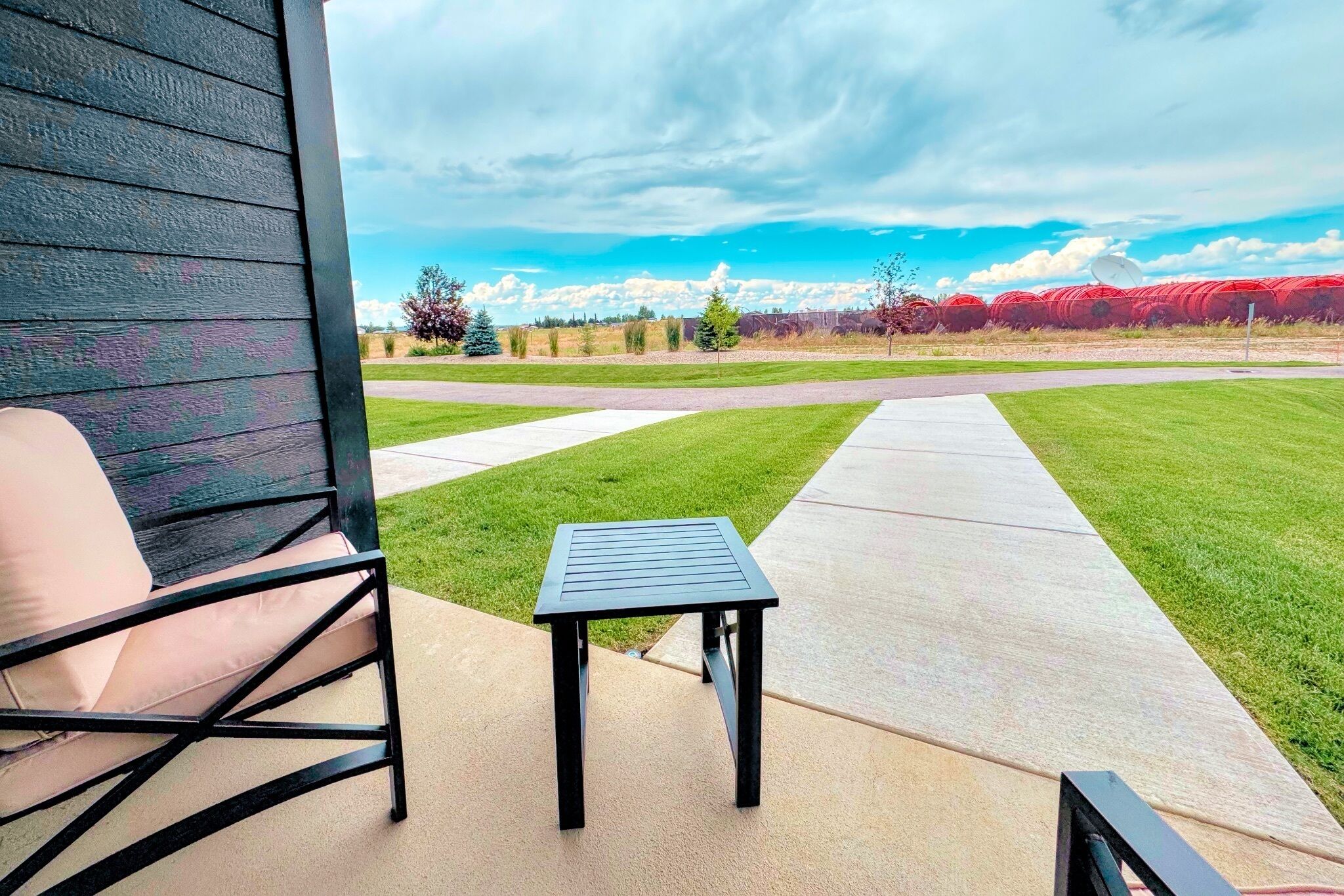 Un espace patio avec une table et une chaise, un chemin en béton et une vue sur un champ verdoyant et des arbres au loin.