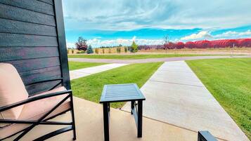 Un espace patio avec une table et une chaise, un chemin en béton et une vue sur un champ verdoyant et des arbres au loin.