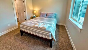 A bedroom with a bed, a nightstand, a lamp, a window, and a door. - Modern Teton Valley Townhome w/AC + Garage (Driggs)