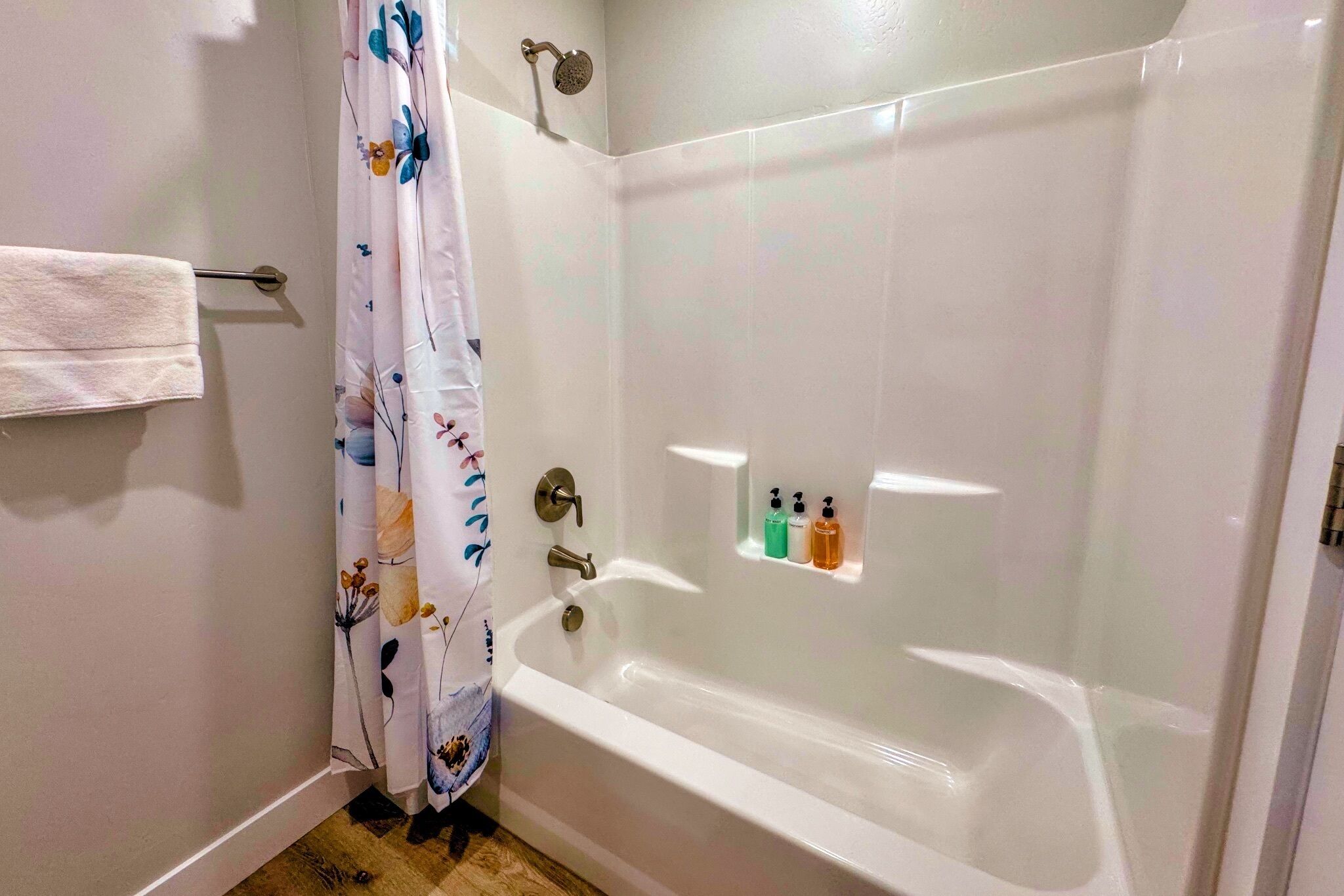 A bathroom with a bathtub, a shower, a towel rack, and a shelf with toiletries.