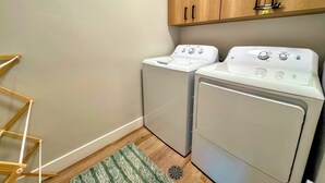 A laundry room with two white washing machines, wooden cabinets, a green striped rug, and a wooden ladder. - Modern Teton Valley Townhome w/AC + Garage (Driggs)