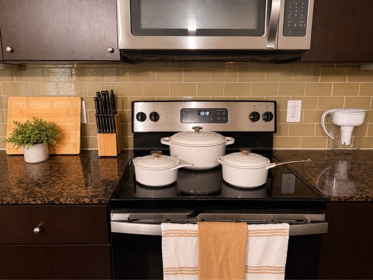 A kitchen with a stove, pots, a microwave, and a countertop with a plant and knives.
