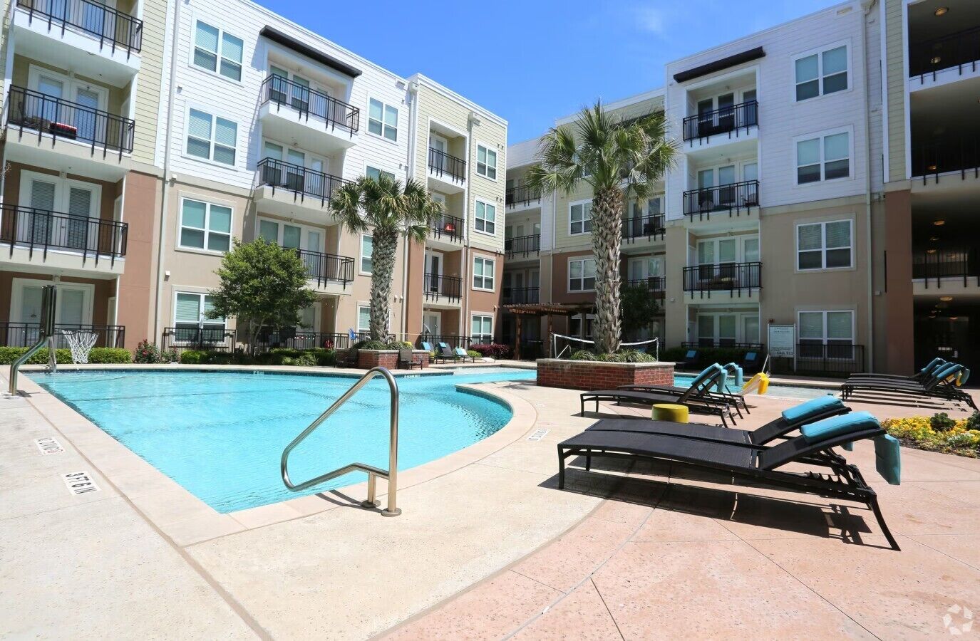 A swimming pool with lounge chairs and a basketball hoop, surrounded by multi-story residential buildings.