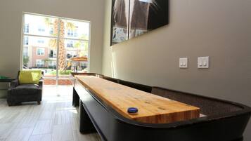 Une table de jeu de « shuffleboard » dans une pièce donnant sur un bâtiment à l’extérieur.