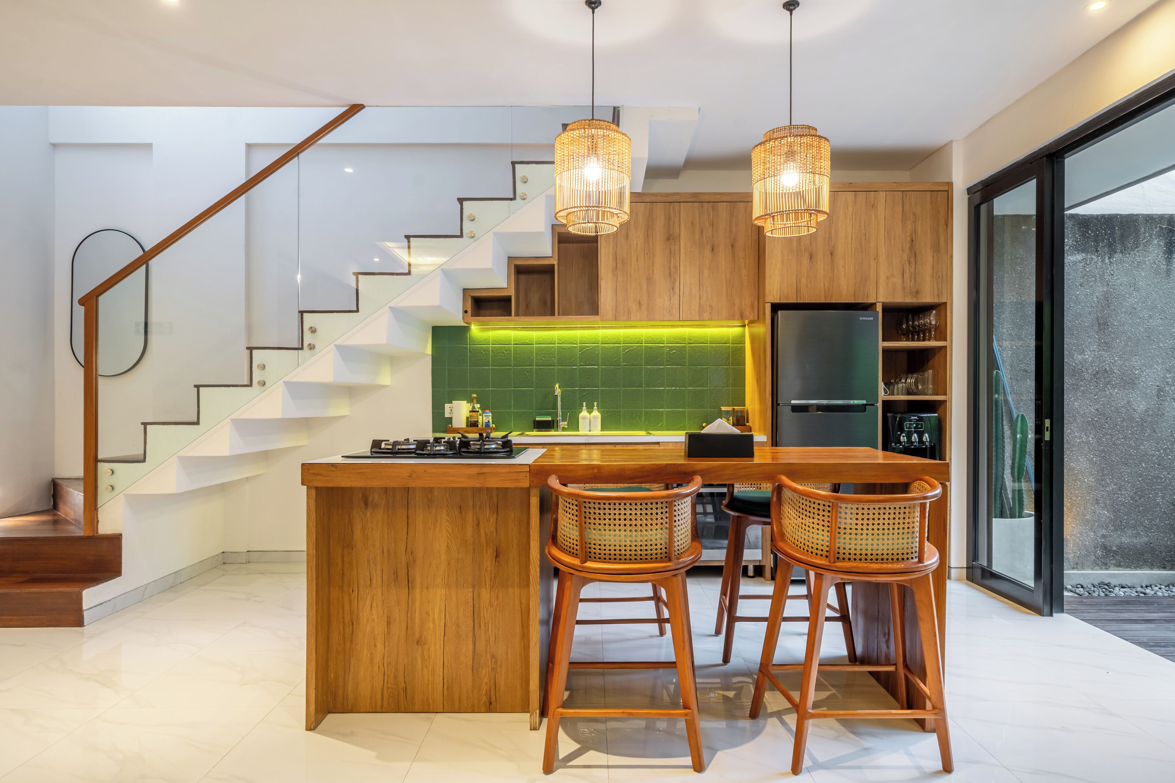 A modern kitchen with a central island, wooden bar stools, and a staircase with glass railings.