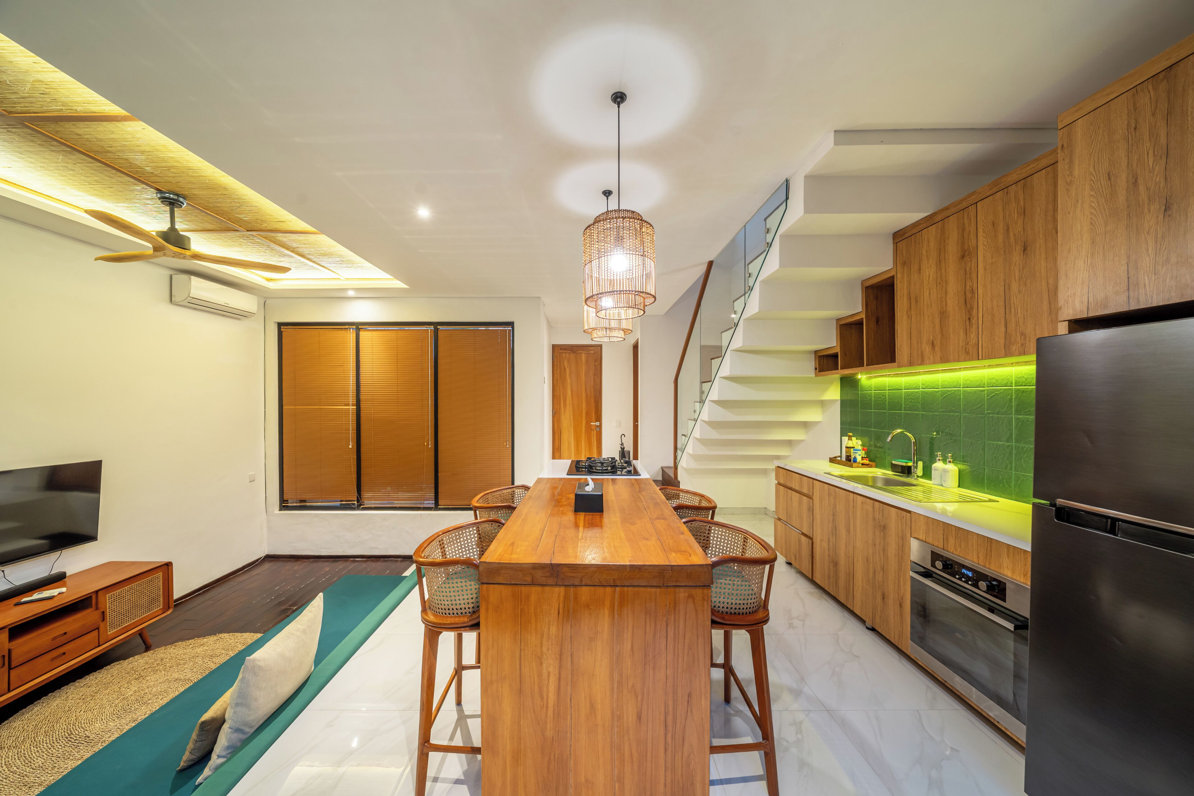 A modern kitchen with wooden cabinets, a central island, bar stools, a built-in oven, and a television.
