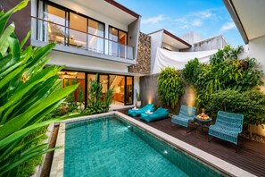 A modern outdoor pool area with a wooden deck, lounge chairs, and a view of a two-story building with large windows. - Villa Lula 2BR Canggu & Rice Field Views (Badung)