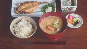 Comida con arroz, sopa y pescado sobre una mesa de madera.