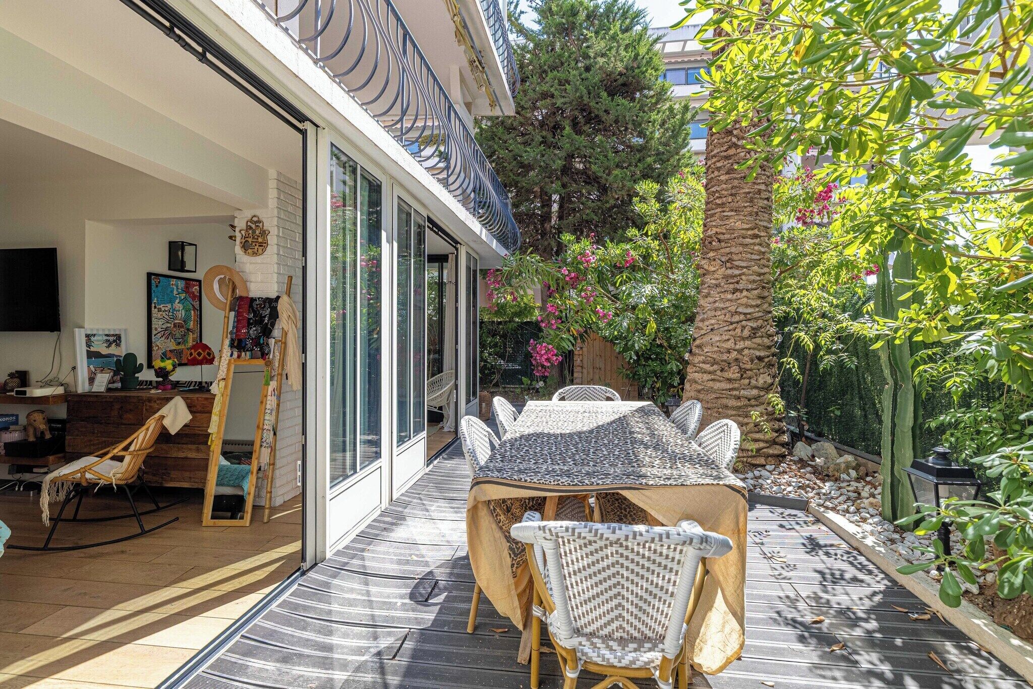 Un espace extérieur aménagé avec une table et des chaises, une terrasse en bois, ainsi qu’une variété de plantes et d’arbres.