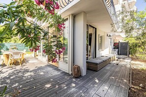 Eine Holzterrasse mit Gartenmöbeln, einer überdachten Sitzgruppe und Blick auf ein Gebäude mit Balkonen.