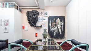 Una galeria d'art amb una taula de vidre, cadires i diverses obres d'art a les parets.