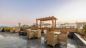 A rooftop terrace with wicker furniture and a pergola, featuring a cityscape view. - Hotel Golden Place 377 (Gurugram)