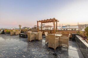 A rooftop terrace with wicker furniture and a pergola, featuring a cityscape view. - Hotel Golden Place 377 (Gurugram)