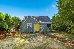 A single-story house with a yellow front door, surrounded by trees and a grassy yard. - Freshly renovated home with brand-new appliances, a new big-screen TV, refinished hardwood floors, and all-new furniture throughout. Sink into the plush leather sectional (pull-out queen sleeper) or dine at the six-seat table in the garden. (Vancouver)
