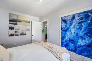 Ein Schlafzimmer mit einem Bett, einer Tür und einem großen Fenster mit einem blauen, abstrakten Gemälde.