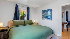 A bedroom with a large bed, a window with curtains, a nightstand with a lamp, and a painting on the wall. - Freshly renovated home with brand-new appliances, a new big-screen TV, refinished hardwood floors, and all-new furniture throughout. Sink into the plush leather sectional (pull-out queen sleeper) or dine at the six-seat table in the garden. (Vancouver)