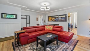 A modern living room with a red leather sectional sofa, a black coffee table, and a patterned rug. - Freshly renovated home with brand-new appliances, a new big-screen TV, refinished hardwood floors, and all-new furniture throughout. Sink into the plush leather sectional (pull-out queen sleeper) or dine at the six-seat table in the garden. (Vancouver)