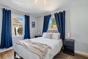 A bedroom with a bed, nightstands, a lamp, and curtains. - Freshly renovated home with brand-new appliances, a new big-screen TV, refinished hardwood floors, and all-new furniture throughout. Sink into the plush leather sectional (pull-out queen sleeper) or dine at the six-seat table in the garden. (Vancouver)