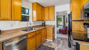 A modern kitchen with wooden cabinets, a stainless steel sink, and a built-in oven. - Freshly renovated home with brand-new appliances, a new big-screen TV, refinished hardwood floors, and all-new furniture throughout. Sink into the plush leather sectional (pull-out queen sleeper) or dine at the six-seat table in the garden. (Vancouver)