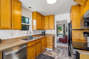 A modern kitchen with wooden cabinets, a stainless steel sink, and a built-in oven. - Freshly renovated home with brand-new appliances, a new big-screen TV, refinished hardwood floors, and all-new furniture throughout. Sink into the plush leather sectional (pull-out queen sleeper) or dine at the six-seat table in the garden. (Vancouver)